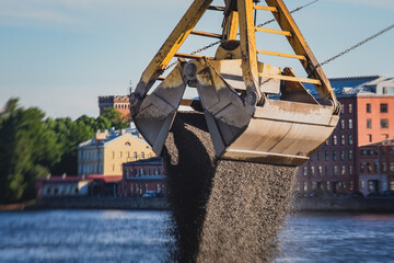 Bulk-handling crane unloading sand, road metal and gravel from cargo vessel ship, heavy vehicle and...