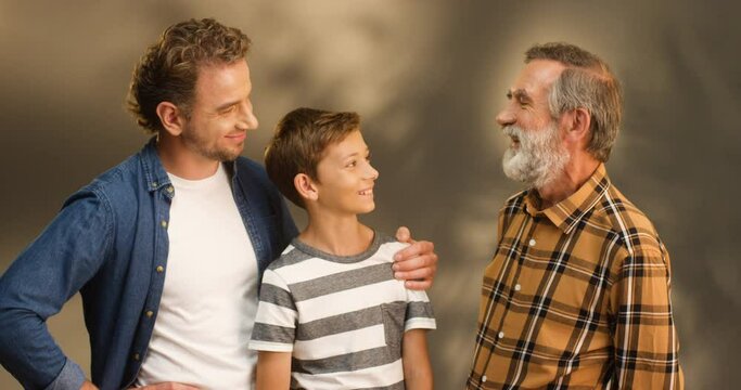 Portrait shot of Caucasian happy male three generations. Young handsome man with teen son and old gray-haired father looking at each other and smiling. Small boy with dad and senior grandfather.