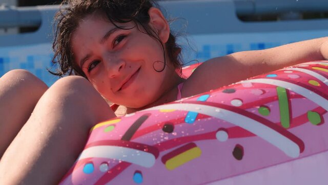 11-12 years old happy cute caucasian girl lying on an inflatable donut circle in the swimming pool in a garden. Cool summer holidays for children and kids. games on the water. Pink donat. 4k slow moti