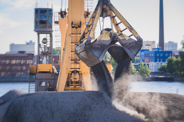 Bulk-handling crane unloading sand, road metal and gravel from cargo vessel ship, heavy vehicle and...