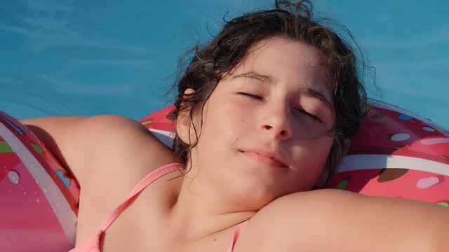 11-12 years old happy cute caucasian girl lying on an inflatable donut circle in the swimming pool in a garden. Cool summer holidays for children and kids. games on the water. Pink donat. 4k slow moti