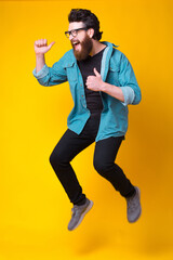 Fototapeta na wymiar Singing or screaming bearded man wearing glasses is jumping over yellow background