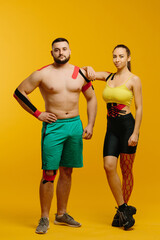 Professional athletes, man and woman with kinesiological tape on the body, posing on a yellow background. Sports and rehabilitation, kinesiotherapy treatment