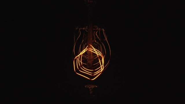 Flickering Tungsten light bulb lamp on black background. Periodic dimming of vintage Edison light bulbs in darkness. Electricity problem or horror movie concept.
