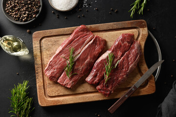 Two raw marbled ribeye steak on cutting board with rosemary on black background. Top view. Top view flat lay with copy space