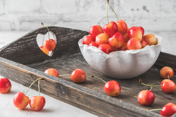 White bowl with ripe orange sweet cherries of sort 'royal anne' on a wooden tray, white background