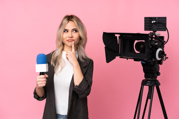 Reporter woman holding a microphone and reporting news over isolated pink background scheming...