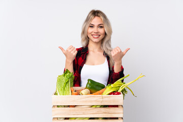 Farmer girl holding a basket full of fresh vegetables over isolated white background with thumbs up...