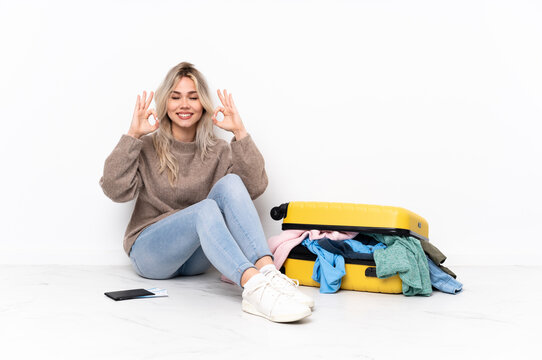 Teenager blonde girl with a suitcase full of clothes sitting on the floor in zen pose
