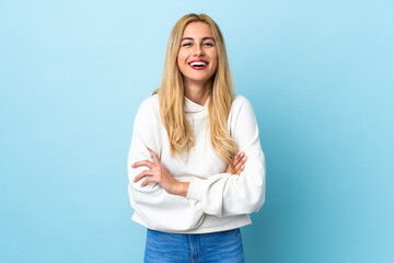 Young Uruguayan blonde woman over isolated blue background keeping the arms crossed in frontal...