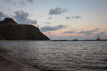 Fototapeta na wymiar A beach at sunset with a ship in the background and hillside on the left