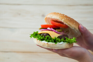 Hands holding homemade beef burger on wooden table. Ready to eat tasty fast food hamberger. Unhealthy food concept.