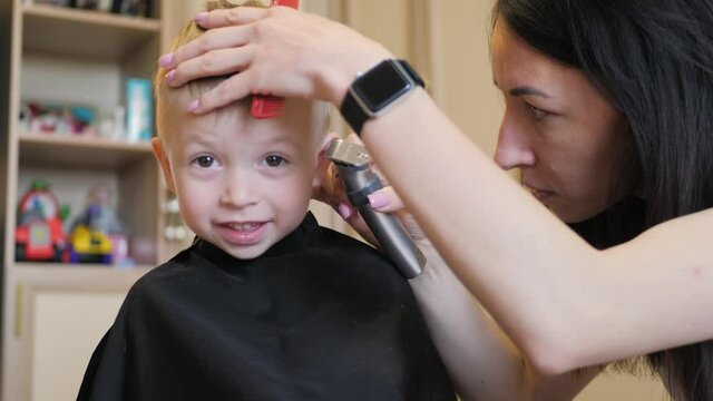 Mom is cutting her little son hair at home.