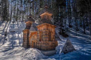 Wooden Russian orthodox chapel dedicated to Saint Vladimir on a sunny winter day, located in forest under the mountain in Slovenia. Landscape covered in snow