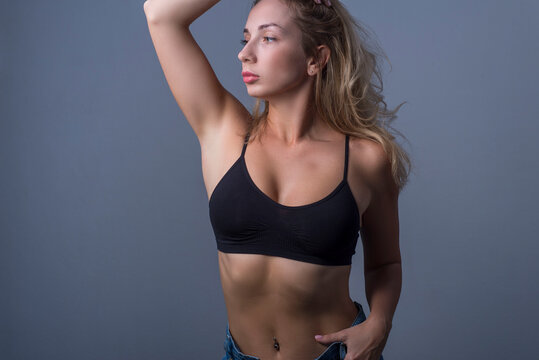 studio portrait of a young beautiful blonde girl, twenty-eight years old. In jeans and a black bra top. Advertising photo on a gray background. Free space.