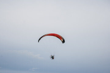 Piloto voando com paramotor vermelho em céu nublado em Goiânia.