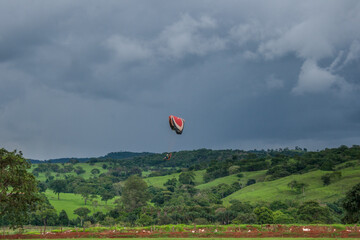 Paramotor voando em campo com céu nublado ao fundo.