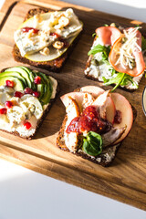 Four different rye bread open sandwiches (avocado-quail eggs, pear-gorgonzola, ham-cheese, turkey-apple) on wooden board on white background.