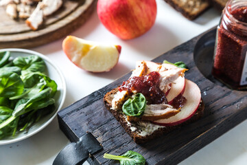 Open sandwich with rye bread, roasted turkey , cream cheese, apple and cranberry sauce and sauce jar on wooden board and sandwich ingredients  on white background. 