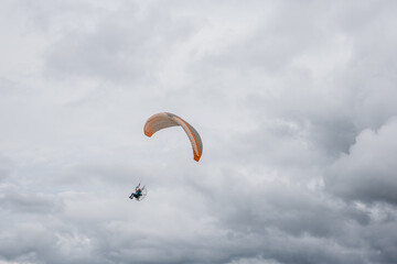 Pessoa voando de paramotor em céu nublado.