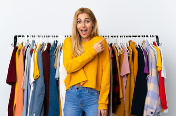 Young Uruguayan blonde woman in a clothing store surprised and pointing side