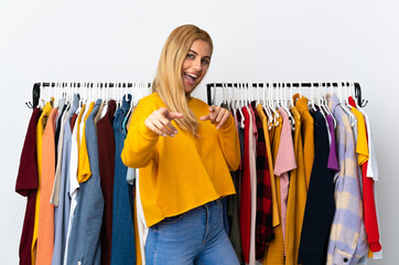 Young Uruguayan blonde woman in a clothing store pointing to the front and smiling