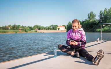 Fototapeta premium Active girl browsing music on her phone during workout outdoors