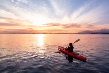 Sea Kayaking in calm waters during a colorful and vibrant sunset. Adventure Girl in Red Kayak. Location: White Rock, Vancouver, British Columbia, Canada.