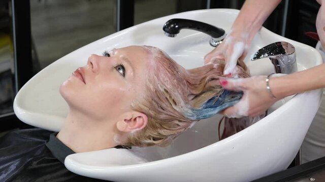 The hairdresser washes off the paint with a blond hair client in a beauty salon. Studio hairdresser.