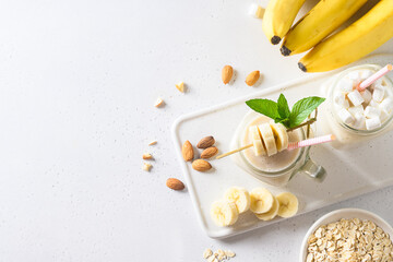 Banana milkshake with oatmeal and almond nuts in mason jar on white board. View from above. Space for text.