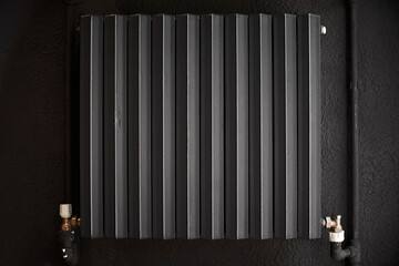 Cast iron radiator heater for home. Black heating battery on the black wall