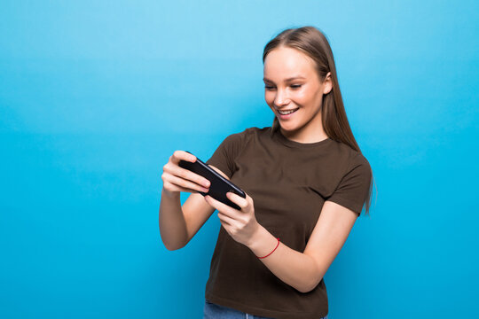 Excited nice woman playing video game on cellphone and making winner gesture isolated over blue background