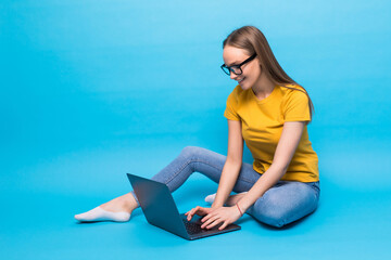 Attractive woman with beautiful smile using silver notebook, while sitting in lotus pose on the floor isolated over blue background