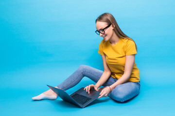 Attractive woman with beautiful smile using silver notebook, while sitting in lotus pose on the floor isolated over blue background