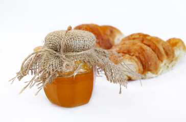 honey in a jar with burlap on a white plate with croissants, food closeup