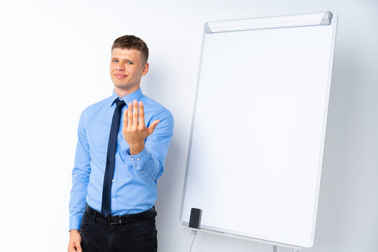 Young businessman giving a presentation on white board inviting to come with hand. Happy that you came