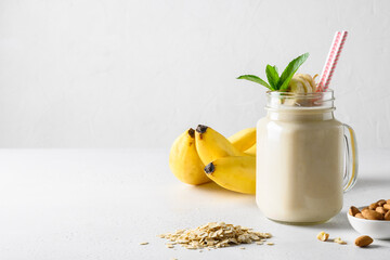 Banana milkshake with oatmeal and almond nuts in mason jar on white board. Space for text. - obrazy, fototapety, plakaty