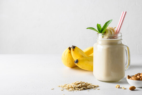 Banana milkshake with oatmeal and almond nuts in mason jar on white board. Space for text.