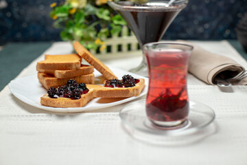 Toast slices with red jam and a glass of tea on the white table