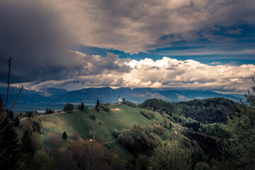 Naklejka na ściany i meble Famous Jamnik church on hilltop in summer season with incoming storm clouds. Picturesque landmark in Slovenia. In background Alps mountain range. Green landscape