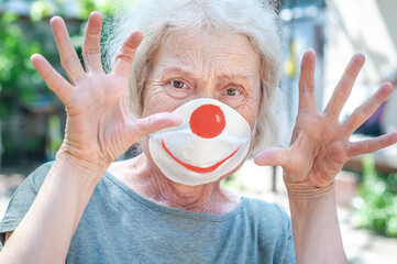 Angry grandmother elderly woman in a respiratory mask with a painted funny clown mask. Tired of...