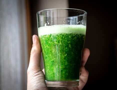 Picture of hand holding glass of green smoothie.
