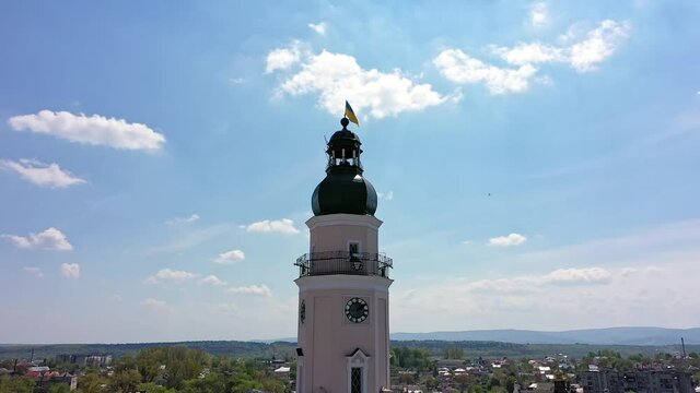 Beautiful town hall with Ukrainian blue and yellow flag rises above the city. Great exterior of historical landmark at central square of old European city Drohobych. 4K Aerial Drone view, pan around