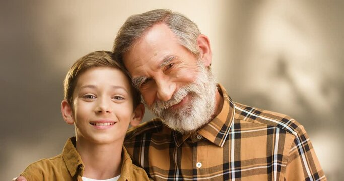 Portrait of Caucasian happy male generations. Old grandfather and grandson looking at each other, turning faces to camera and smiling. Small boy with senior man in hugs. Embracing grandpa.