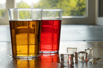 Red and black tea and lemonade in a transparent glass with ice on a background of a sunny window.