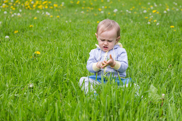 Young blonde girl standing on the green grass.