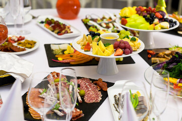 cheese plate on a table with fruits and other dishes with meat and hand-sliced on a banquet table