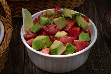 Avocado and tomato salad bowl in white ceramic dish on wooden table