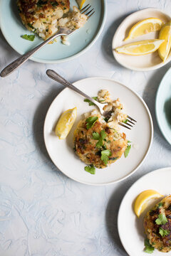 Servings of fried fish cakes with lemon on plates.
