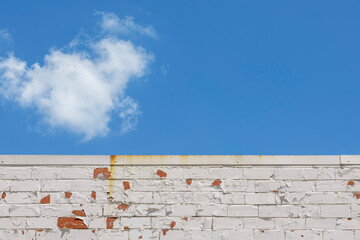 Top of an Orange Brick Wall with Peeling White Paint under a Blue Sky with Clouds